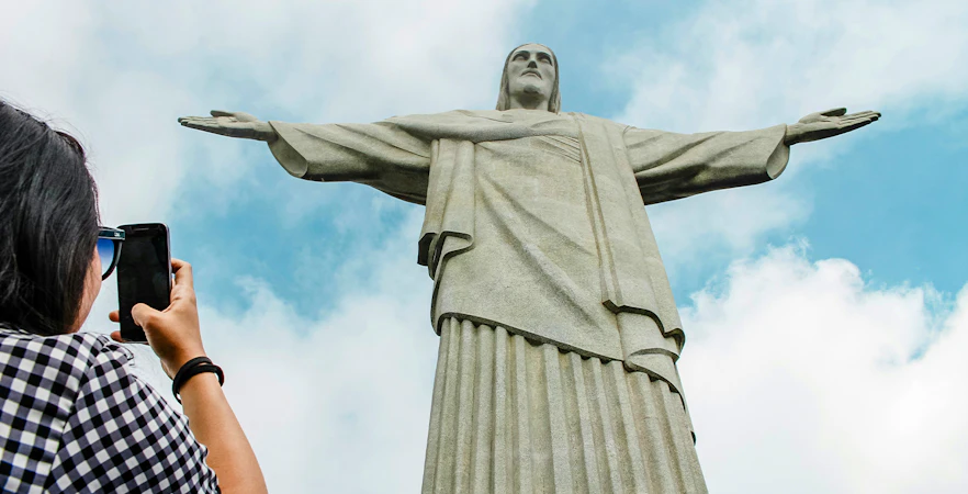 Christ the Redeemer statue in Rio de Janeiro with visitor taking photo.