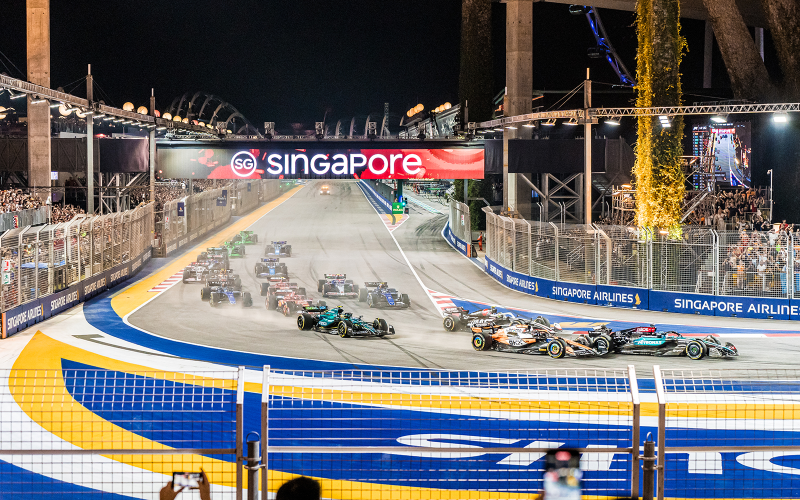 F1 cars racing at Singapore Turn 2 Grandstand during night event.