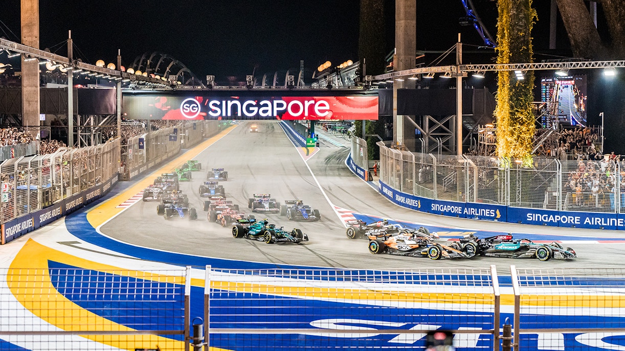 F1 cars racing at Singapore Turn 2 Grandstand during night event.