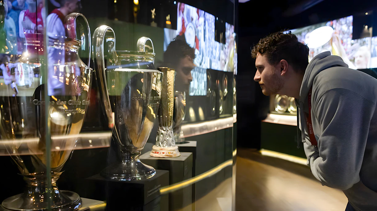 Visitor examining trophies at Johan Cruijff ArenA Classic Tour exhibit.