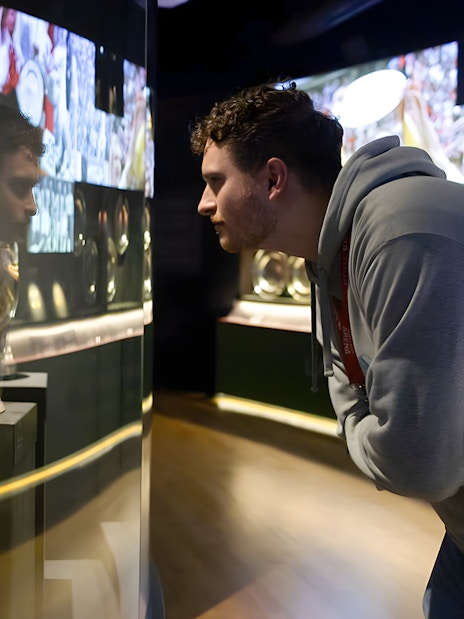 Visitor examining trophies at Johan Cruijff ArenA Classic Tour exhibit.