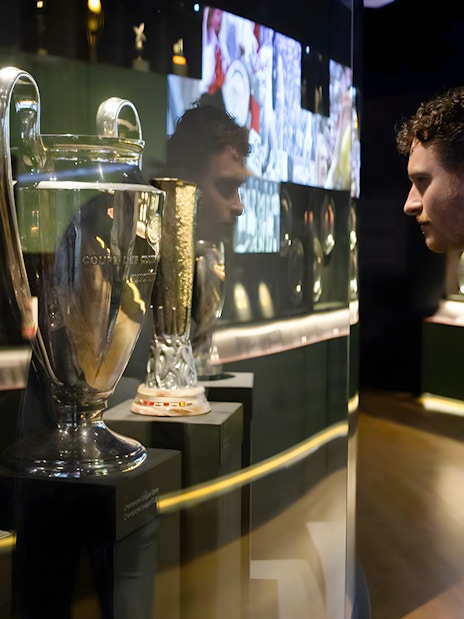 Visitor examining trophies at Johan Cruijff ArenA Classic Tour exhibit.