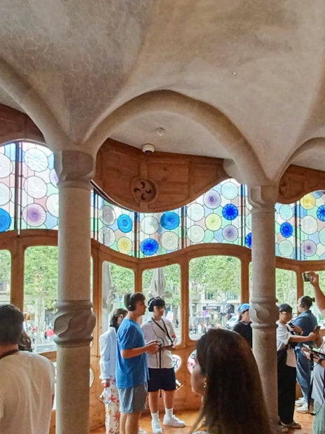 Visitors inside Casa Batlló admiring colorful stained glass windows.