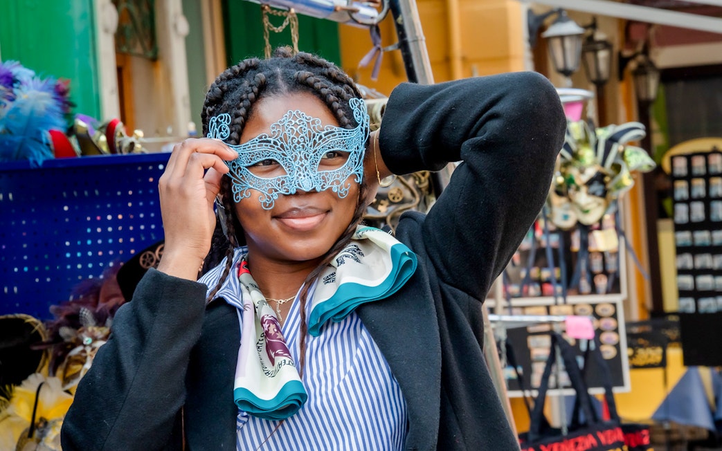 Person holding a decorative mask in a Venetian market.
