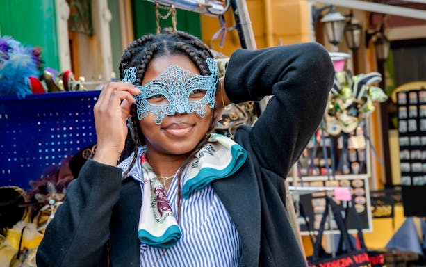 Person holding a decorative mask in a Venetian market.