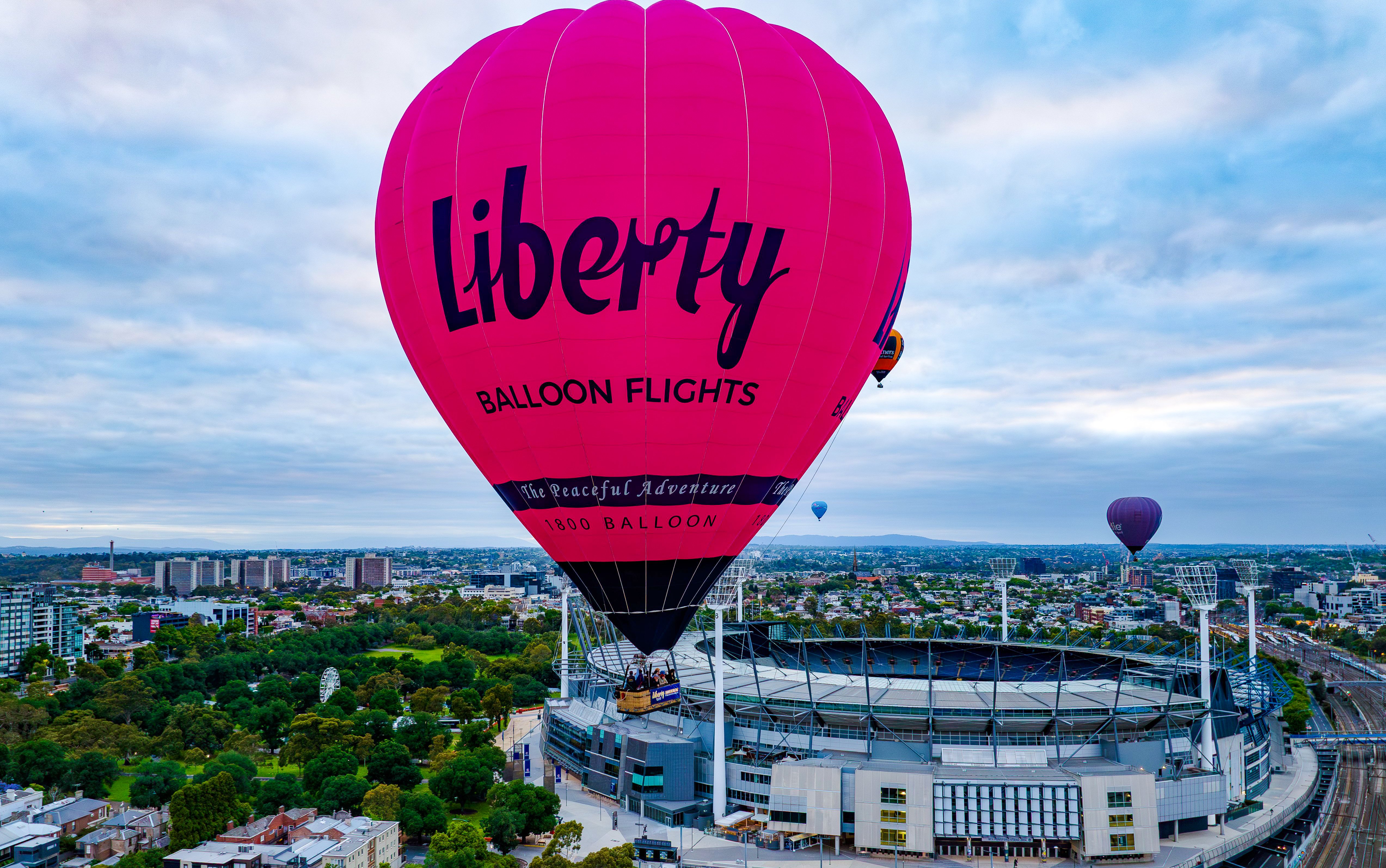 Hot air balloon flying over Melbourne cityscape at sunrise.