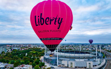 Hot air balloon flying over Melbourne cityscape at sunrise.