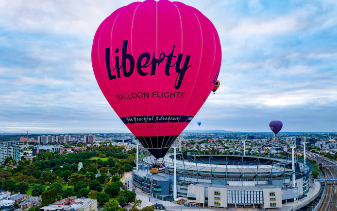 Hot air balloon flying over Melbourne cityscape at sunrise.