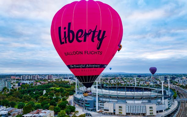 Hot air balloon flying over Melbourne cityscape at sunrise.