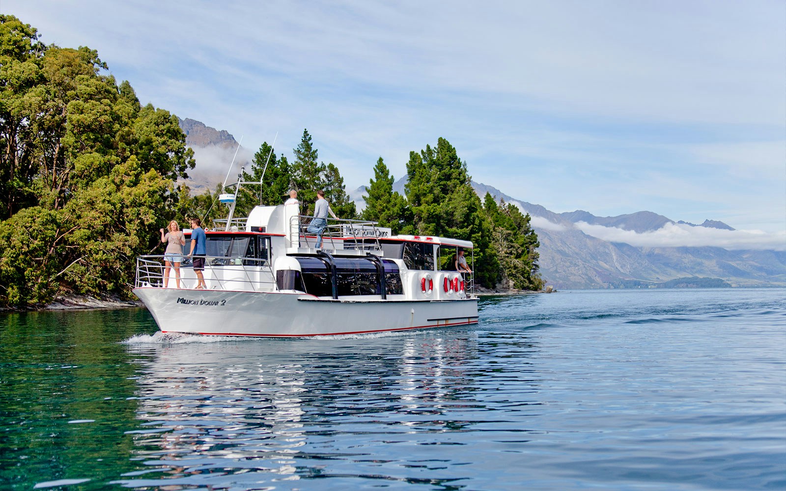 Million Dollar 2 tour boat cruising Lake Wakatipu near Queenstown, New Zealand with forested shoreline.