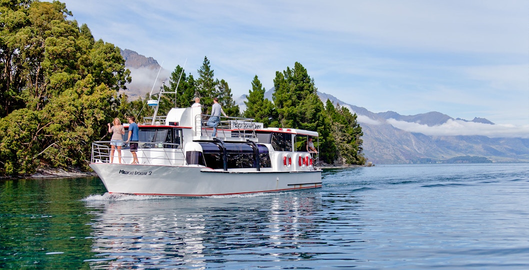 Million Dollar 2 tour boat cruising Lake Wakatipu near Queenstown, New Zealand with forested shoreline.