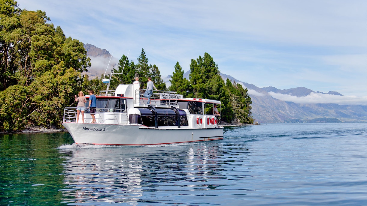 Million Dollar 2 tour boat cruising Lake Wakatipu near Queenstown, New Zealand with forested shoreline.