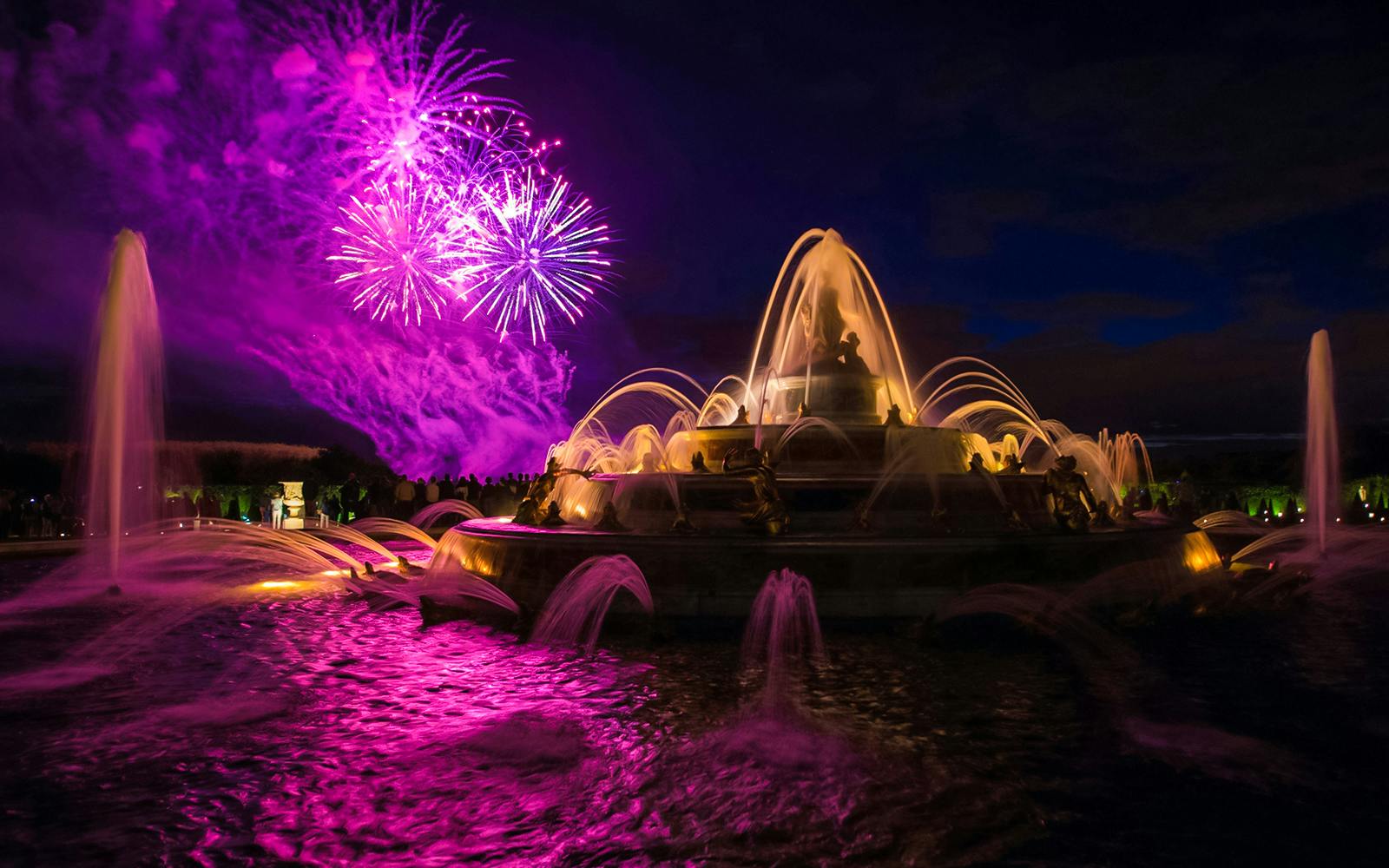 Versailles fountains illuminated with fireworks during night show from Paris.