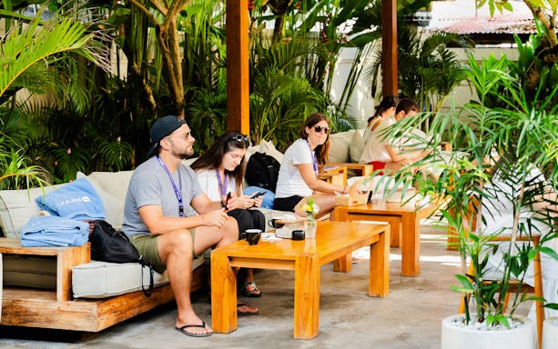 People relaxing at Bluuu Lounge surrounded by lush greenery and wooden furniture.