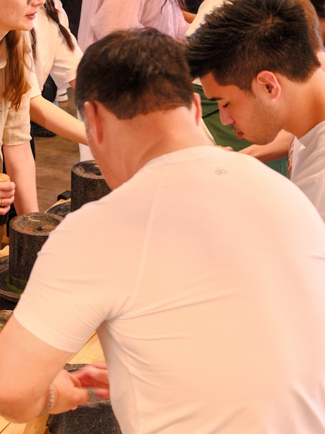 Tourists grinding tencha leaves into matcha powder at Chazuna Museum, Uji, Kyoto.