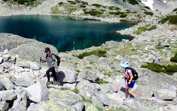 Hikers ascending rocky terrain near a lake on The Seven Rila Lakes tour from Sofia.
