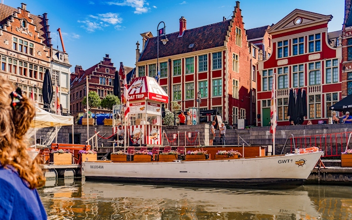 Tourist boat on River Leie at Graslei quay, Ghent, Belgium, with historic buildings.