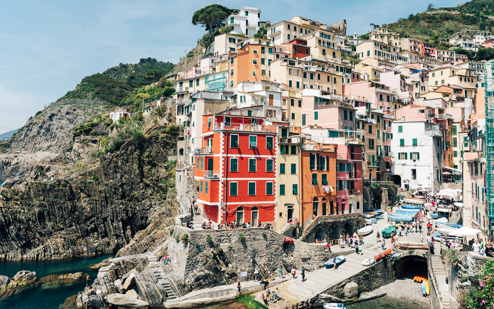 Colorful buildings on cliffs in Riomaggiore, Cinque Terre, with tourists exploring the area.
