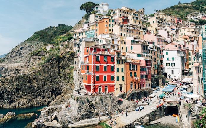 Colorful buildings on cliffs in Riomaggiore, Cinque Terre, with tourists exploring the area.