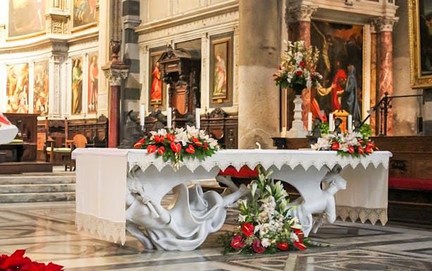 Altar inside Pisa Cathedral adorned with floral arrangements and religious artwork.