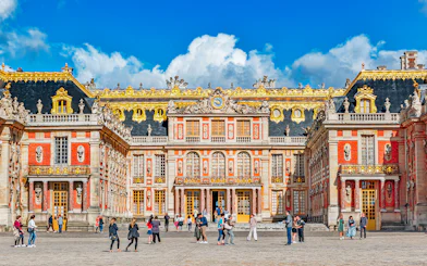Main entrance of Palace of Versailles with visitors exploring the courtyard.