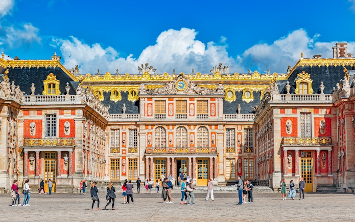 Main entrance of Palace of Versailles with visitors exploring the courtyard.