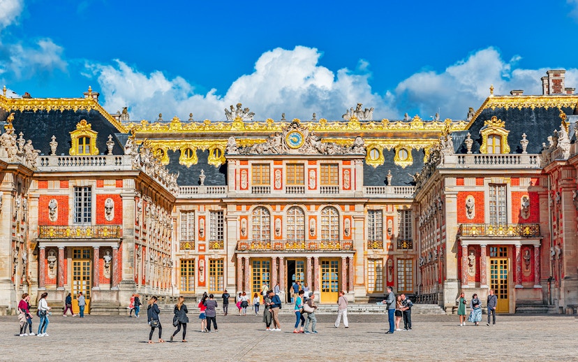Main entrance of Palace of Versailles with visitors exploring the courtyard.