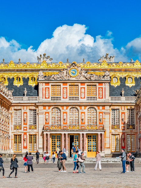 Main entrance of Palace of Versailles with visitors exploring the courtyard.