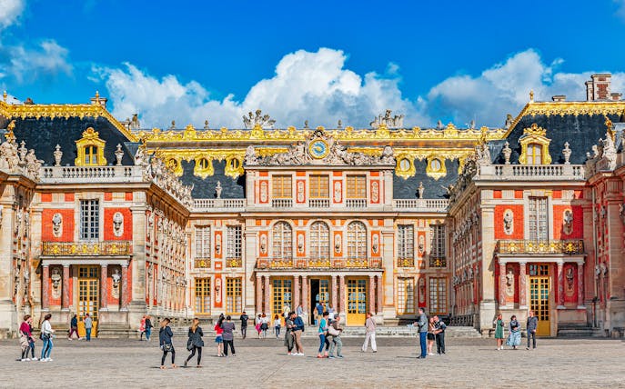 Main entrance of Palace of Versailles with visitors exploring the courtyard.