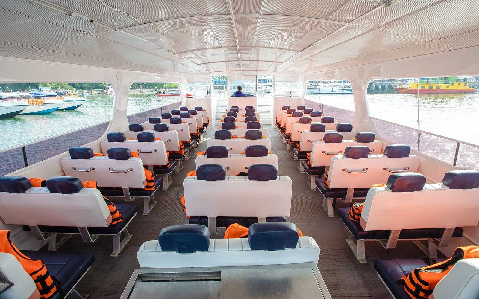 Catamaran interior with rows of seats and life jackets, docked at a marina.