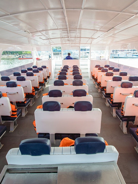 Catamaran interior with rows of seats and life jackets, docked at a marina.