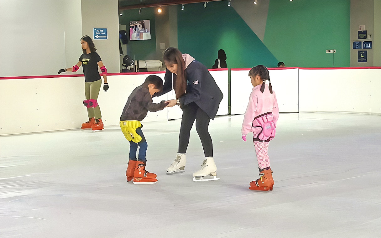 Children learning to ice skate with an instructor at Blue Ice Snow Park.
