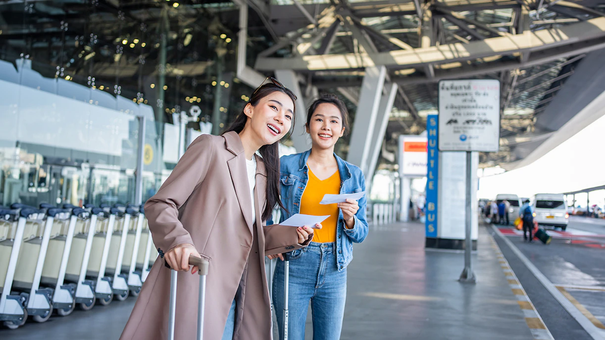 Travelers with luggage at Girona Airport shuttle bus area.
