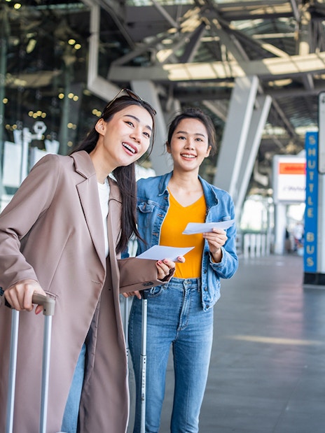Travelers with luggage at Girona Airport shuttle bus area.
