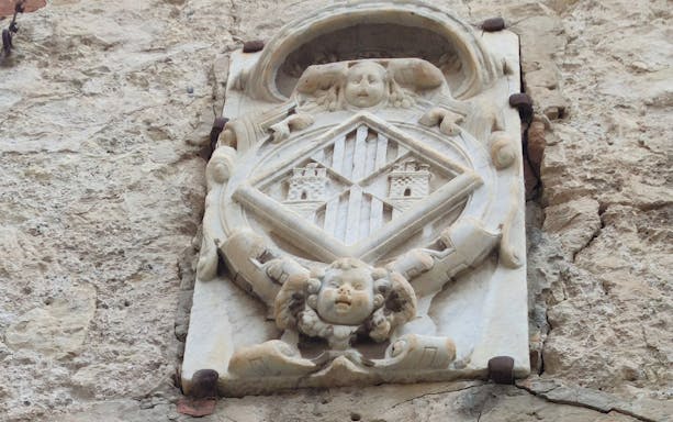 Stone relief with coat of arms on a wall in Castello District, featuring two towers.