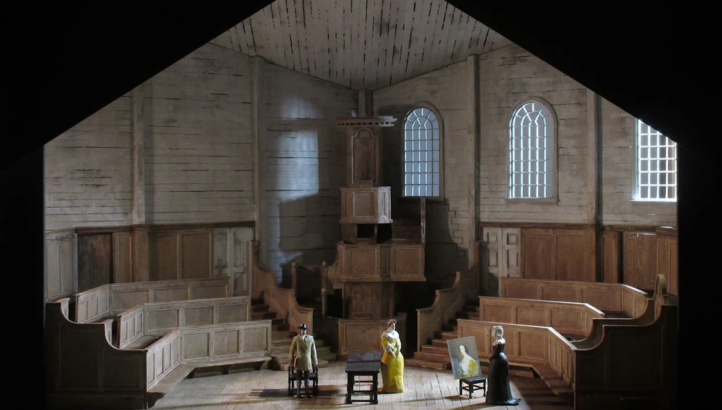 Stage set of "I Puritani" with figures in period costumes in a wooden interior.