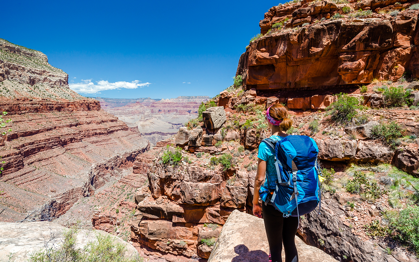 Hiker on a trail overlooking the Grand Canyon's red rock formations.