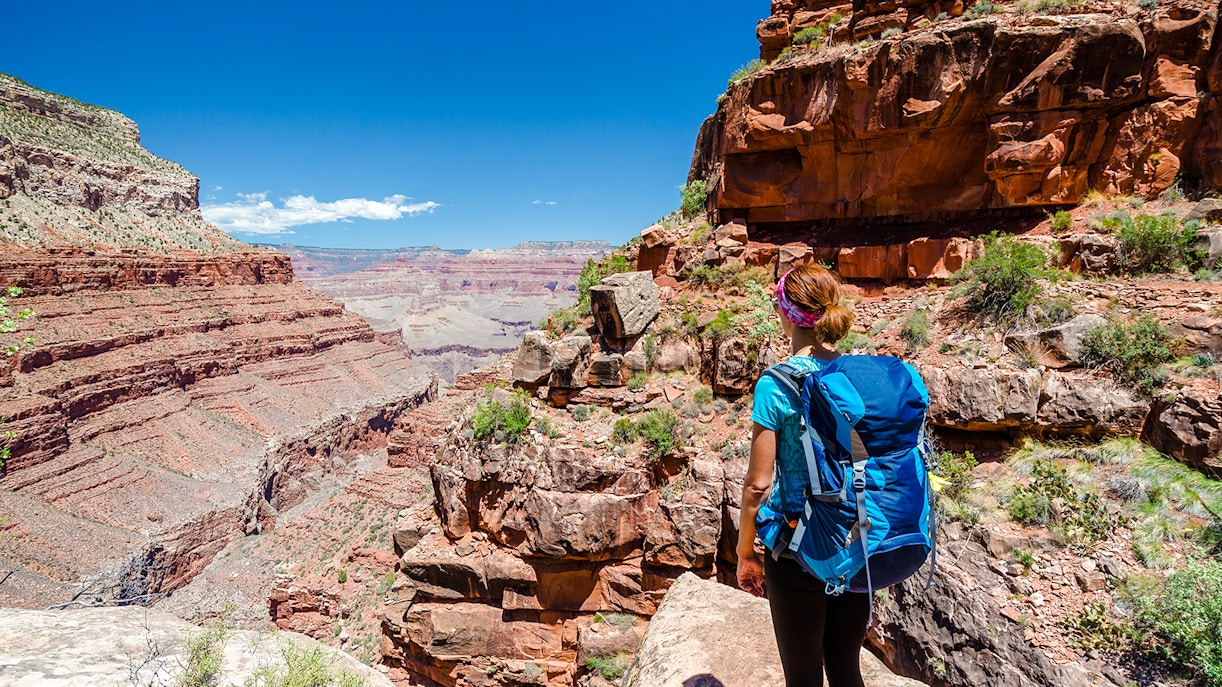 Hiker on a trail overlooking the Grand Canyon's red rock formations.