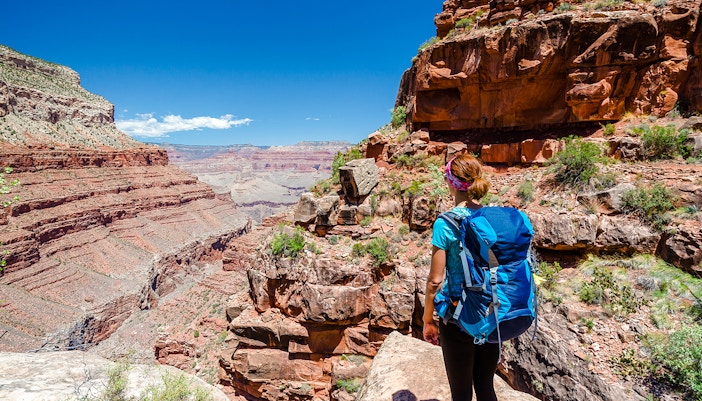 Hiker walking along a scenic trail in the Grand Canyon, surrounded by rugged cliffs and expansive views.