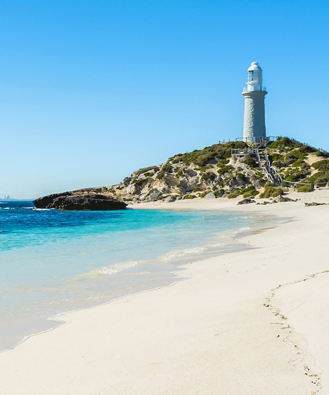 Lighthouse on Pink Beach, Rottnest Island, with clear blue water and sandy shore.