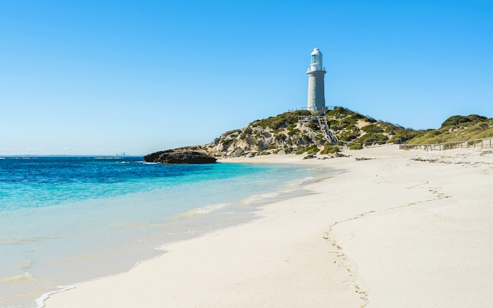 Lighthouse on Pink Beach, Rottnest Island, with clear blue water and sandy shore.