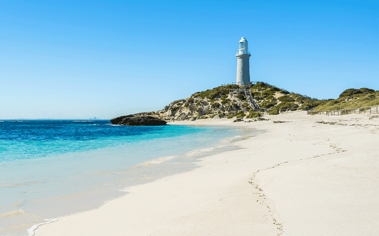 Lighthouse on Pink Beach, Rottnest Island, with clear blue water and sandy shore.