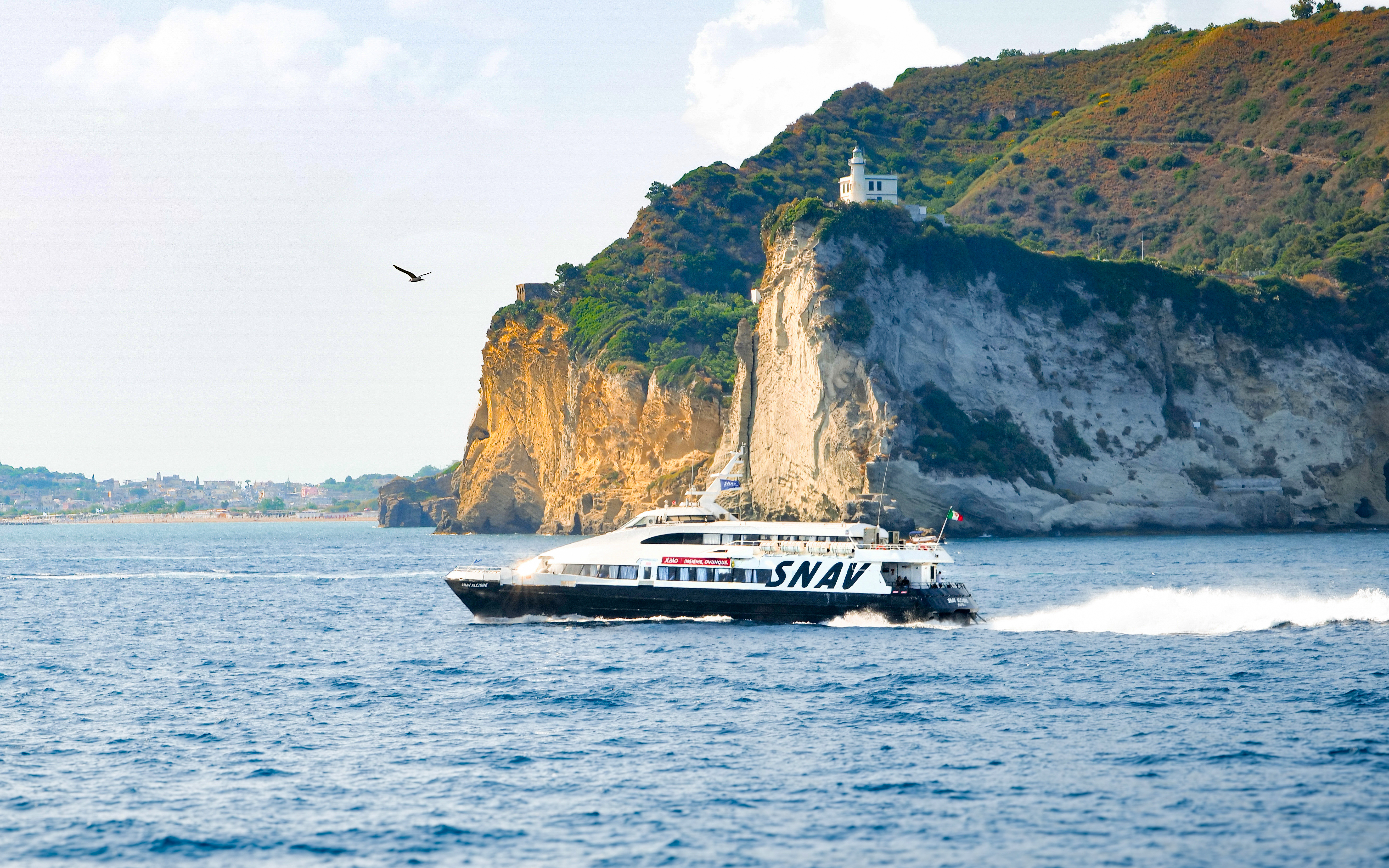 Boat cruising near cliffs on Procida Island tour, Italy.