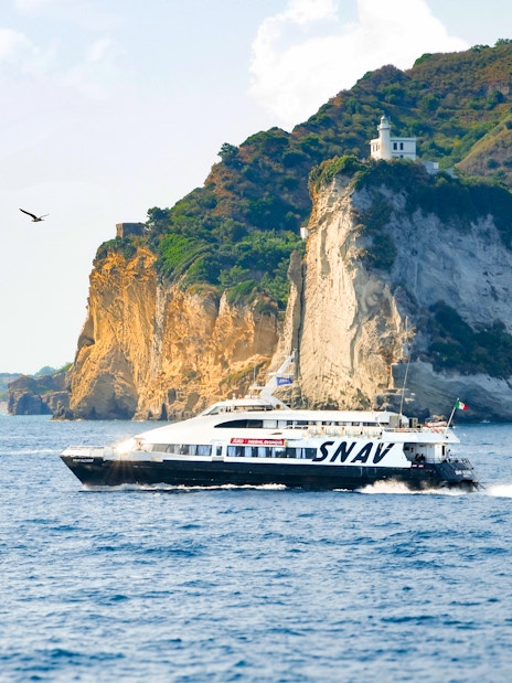 Boat cruising near cliffs on Procida Island tour, Italy.