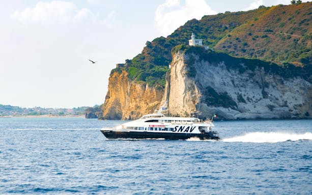 Boat cruising near cliffs on Procida Island tour, Italy.