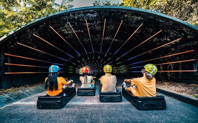 Friends riding luge into colorful tunnel on Skyline Luge, Singapore.