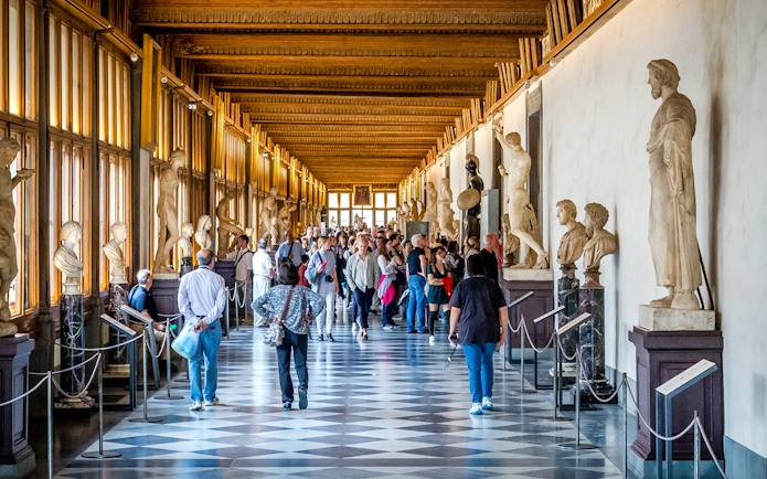 Visitors walking through the statue-lined hallway of the Uffizi Gallery in Florence.