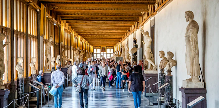 Visitors walking through the statue-lined hallway of the Uffizi Gallery in Florence.