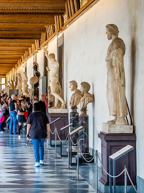 Visitors walking through the statue-lined hallway of the Uffizi Gallery in Florence.