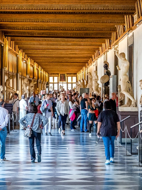 Visitors walking through the statue-lined hallway of the Uffizi Gallery in Florence.